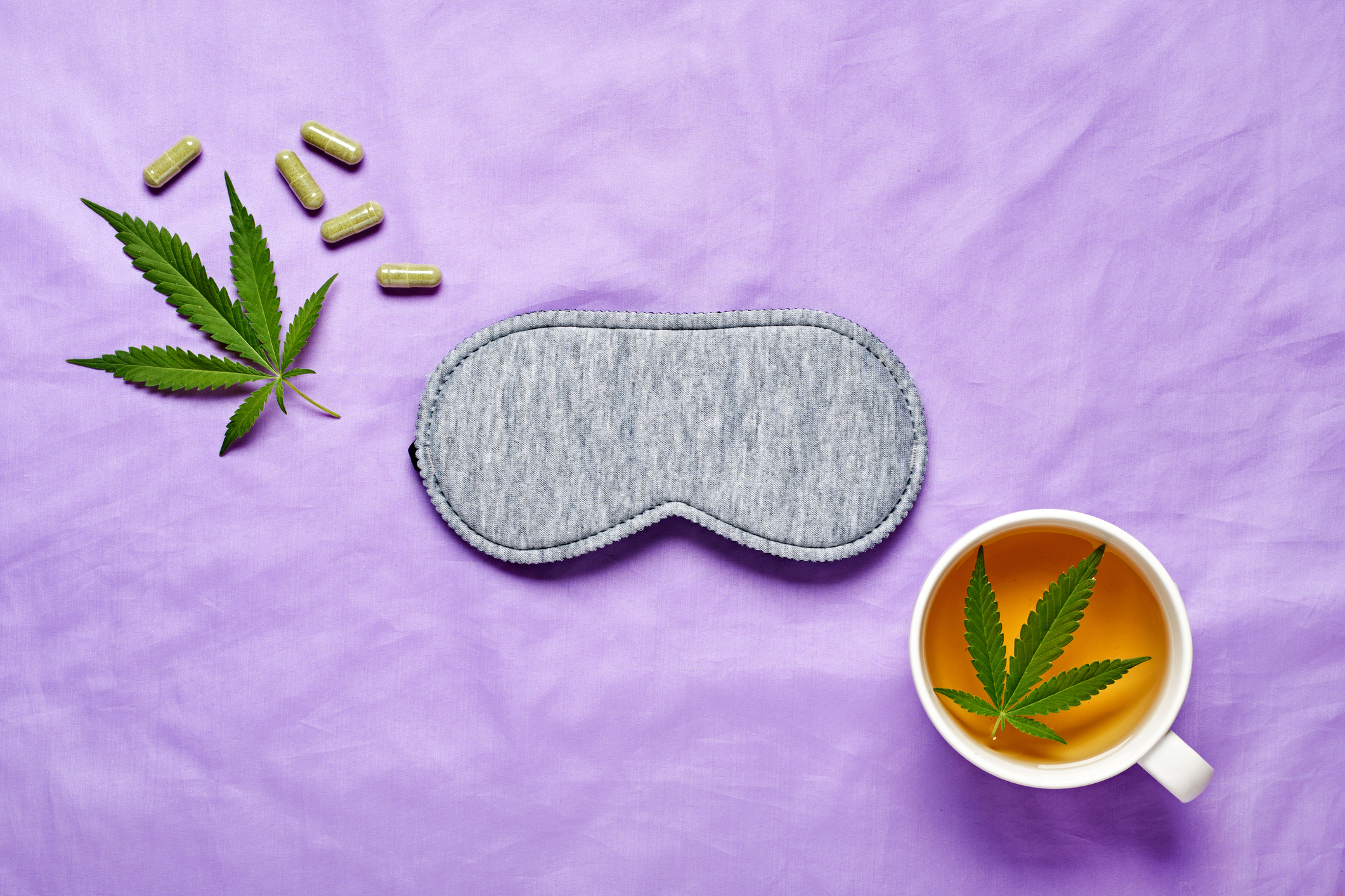 cannabis leaves, weed pills, a sleep mask, and a tea with a cannabis leaf in it to show how cannabis helps sleep
